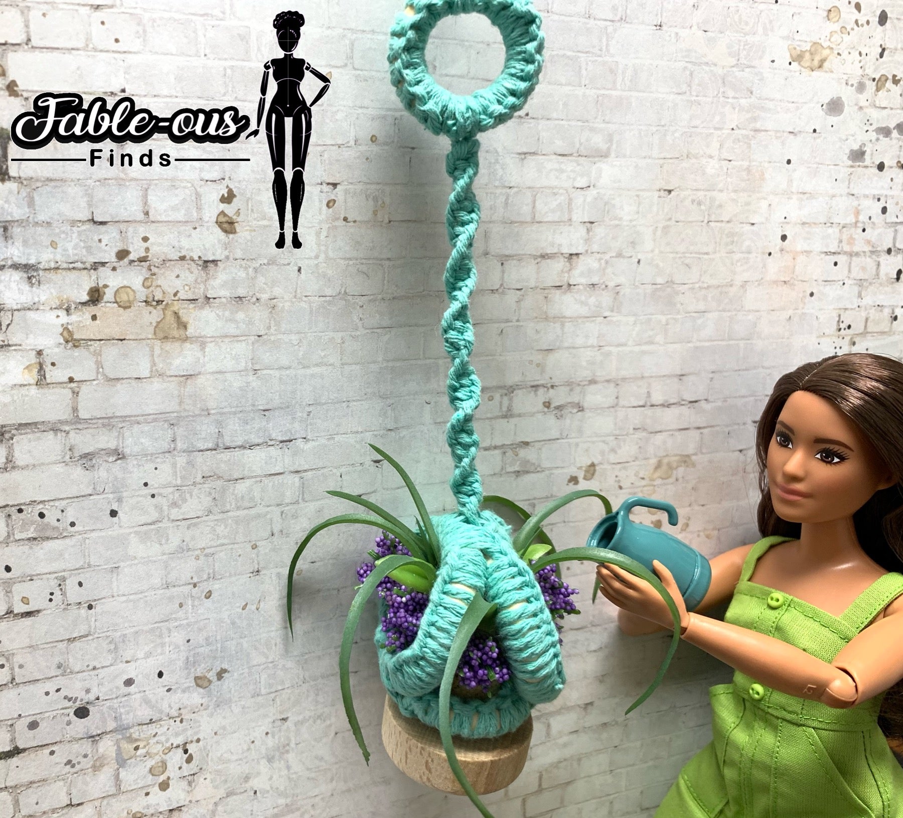 Barbie doll watering a potted plant that is seated in a mini macrame plant hanger.